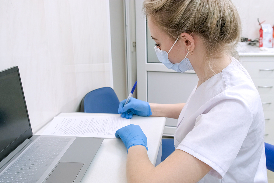 Female medical assistant sitting at a desk with a laptop filling out paperwork