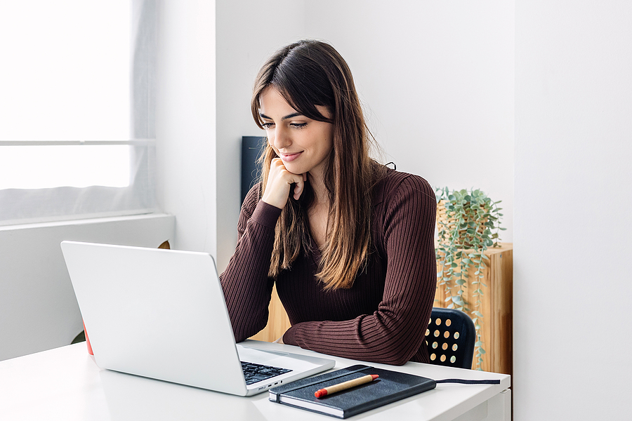 young woman sitting at desk with laptop and notebook studying to become a preschool teacher