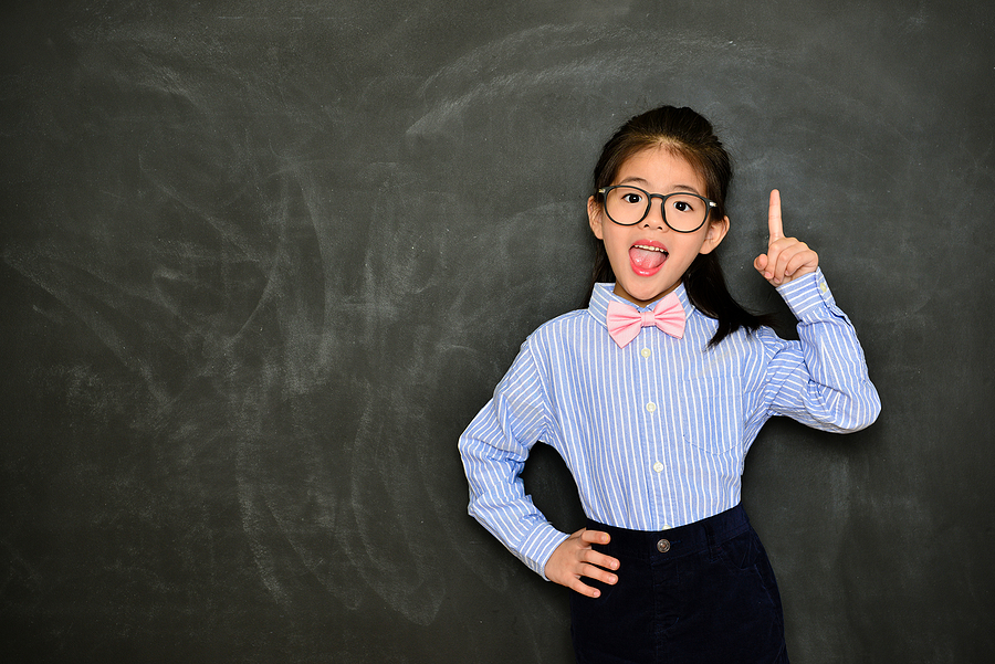 Young student pretending to be the teacher  standing with her back to the chalkboard.