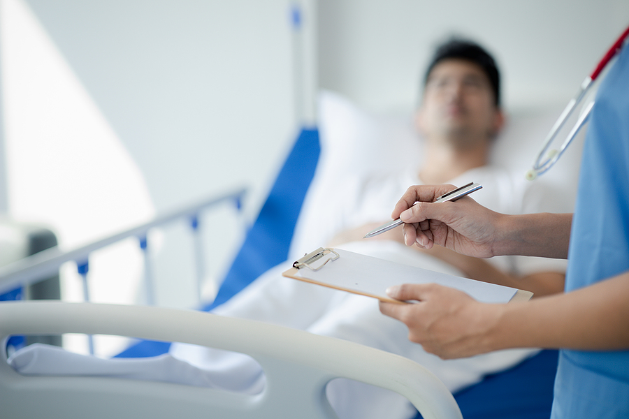 Medical assistant talking to a patient in a hospital bed.