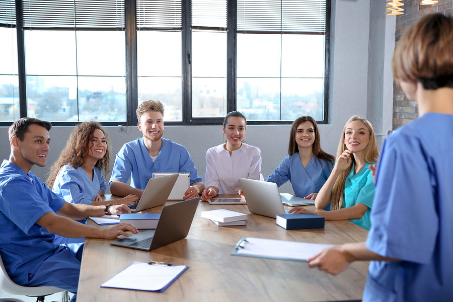 A group of medical assistant students with laptops and clipboards sitting at a table.