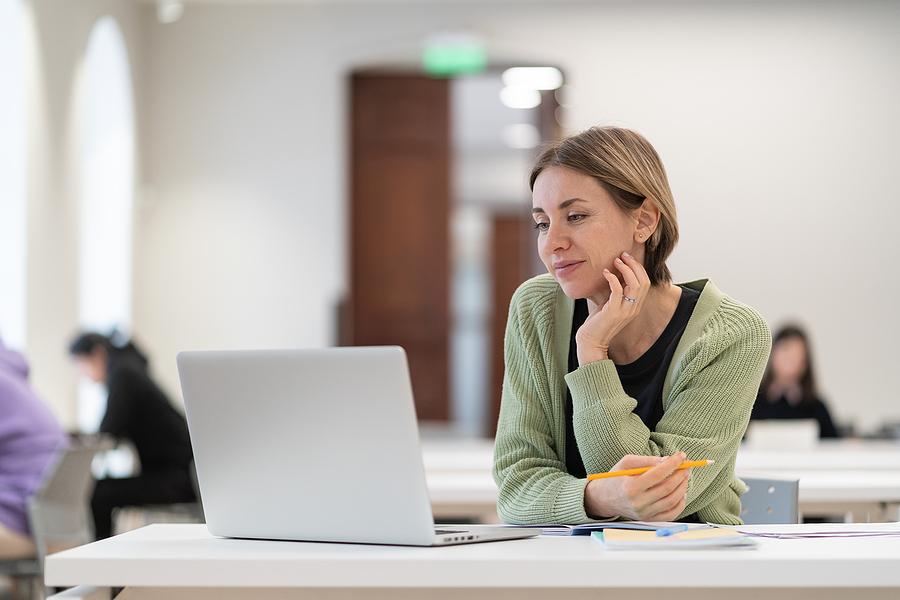 Adult woman sitting at a table with a laptop, pencils, pens, and notebooks