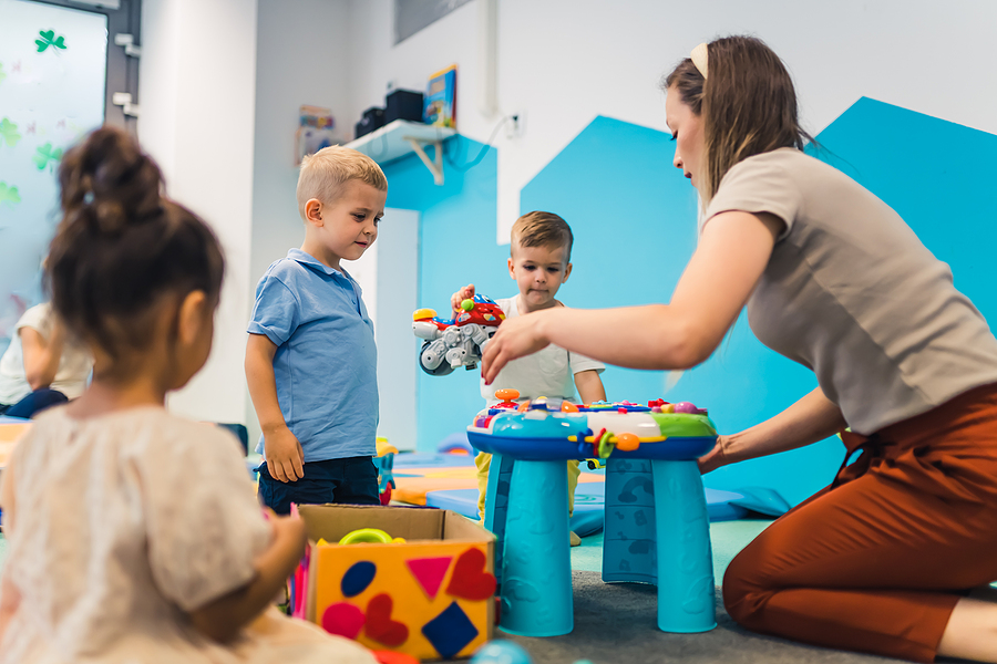 female preschool teacher kneeling on the floor playing with young students