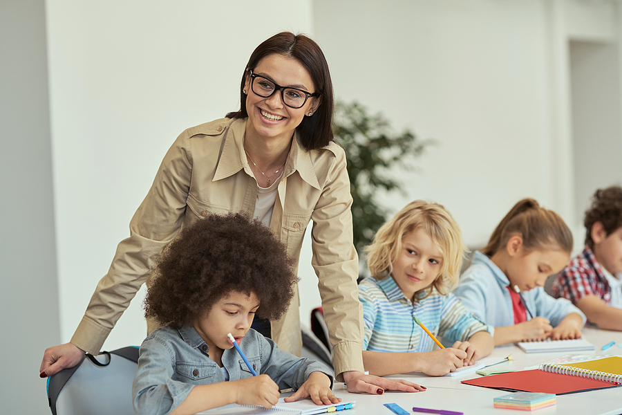 Young preschool teacher helping students at a large classroom table.