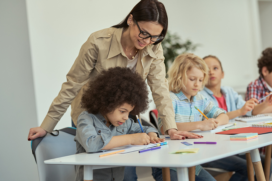 Teacher standing behind a seated student helping them with their class work.
