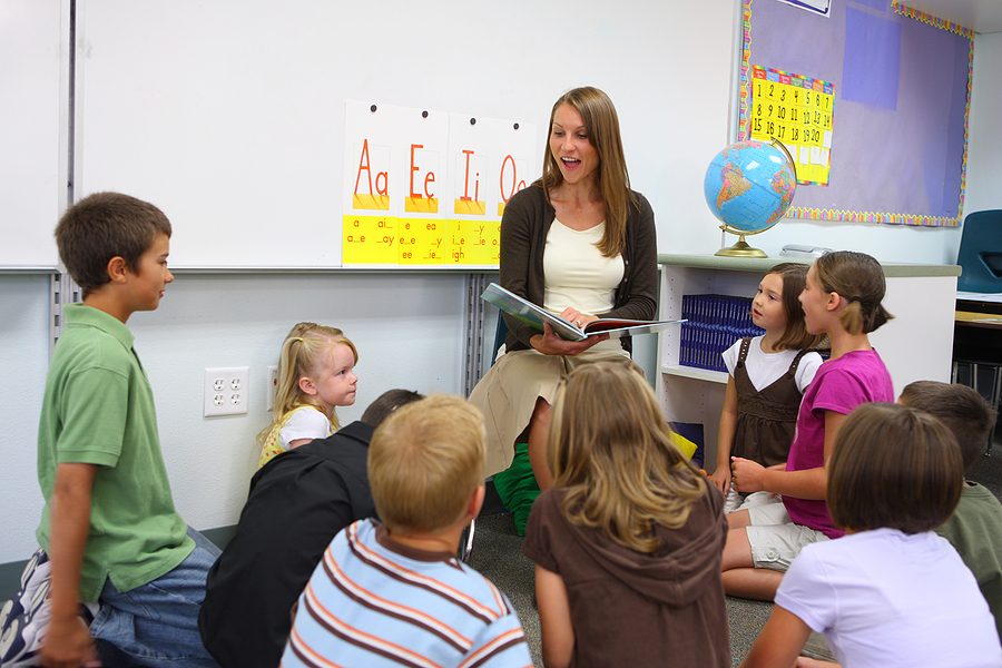 Female early childhood school teacher in a classroom reading to her students