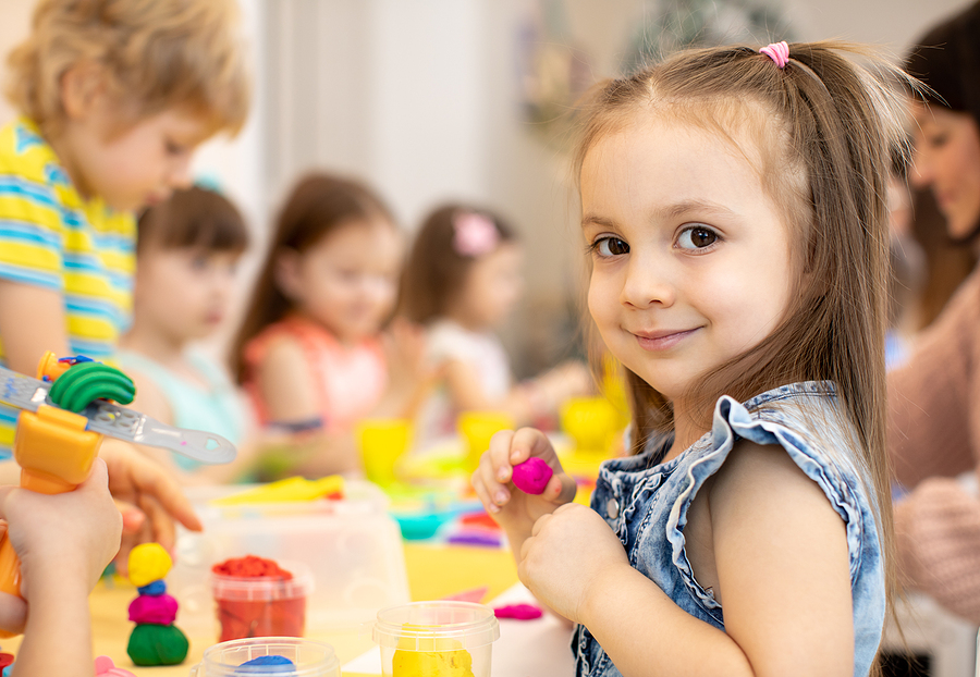 Young preschool student sitting at a classroom table playing with clay.