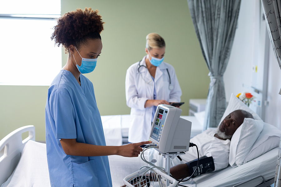 Medical assistant and nurse caring for a patient in a hospital bed.