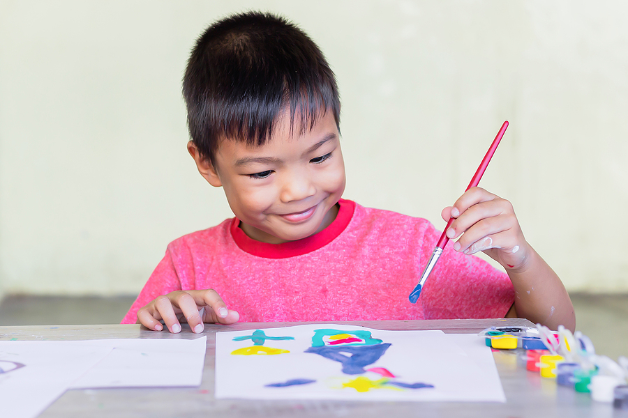Young student painting with watercolors and a paintbrush on white paper.