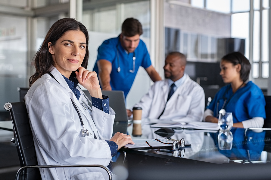 Doctors, nurses, and medical assistants at a table with clipboards and laptops.