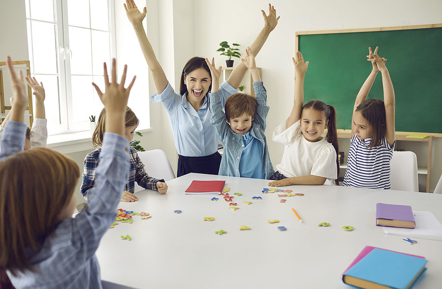 Preschool teacher helping children with a learning activity at a large table.