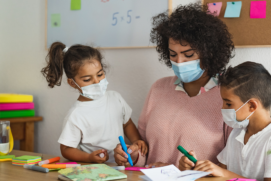Preschool teaching working with two young students, all are wearing masks.