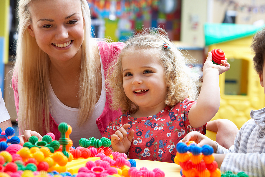 Young blonde preschool teaching working with a little girl in a classroom.