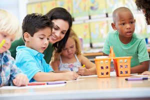 Group of young students with their preschool teacher, seated at a table. 
