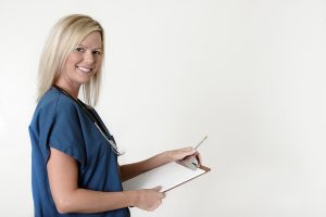 Female medical assistant in blue scrubs is holding a clipboard while smiling at the camera. 