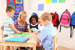 Preschool teacher sitting at a table with her preschool students. 