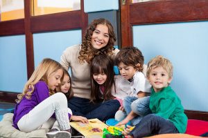 Happy teacher sitting with children on floor in classroom. 