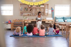 Teacher at montessori school reading to a large group of children on a rug. 