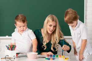 Teacher helping two young students with a painting project. 