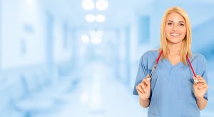 Female nurse wearing blue scrubs and holding a stethoscope around her neck in a medical setting. 