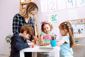Group of young students working with female teacher on a project in an early childhood setting. 
