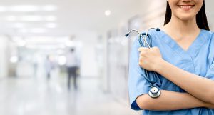 Smiling female nurse wearing blue scrubs, holding a stethoscope. 