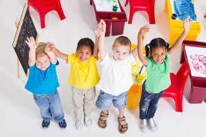 Group of young students standing in a line in a preschool classroom. 