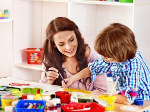 Female preschool teacher helping a student  paint. 