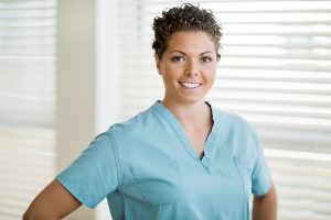 Female nurse wearing light green scrubs standing in a clinic, smiling. 