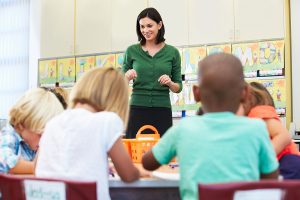 Female teacher standing in front of her classroom teaching to a group of young students. 