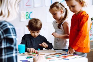 Group of young students working on a project with their female preschool teacher helping. 