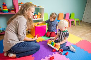 Female early childhood educator supervising an activity with two toddler boys. 