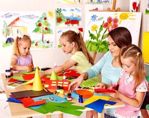 Female preschool teacher helping children with an art project in her preschool classroom. 