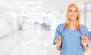 Female nurse wearing blue scrubs and standing in the hallway of a hospital. 