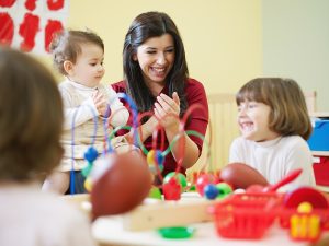Female early childhood educator sitting with young students, engaged in an activity with them. 