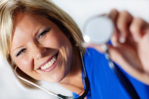 Closeup of a smiling female nurse holding a stethoscope.
