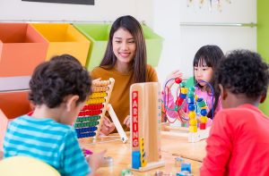 Female preschool teacher sitting at a table with her students. 