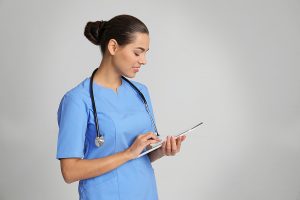 Female nurse wearing blue scrubs and looking something up on a tablet.