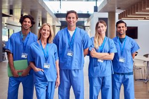 Group of five nurses wearing blue scrubs and standing in a medical facility.