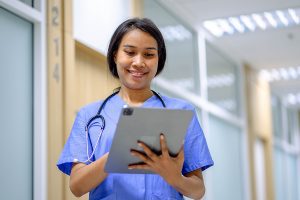 Female nurse wearing blue scrubs and writing something on a digital tablet in a medical clinic. 