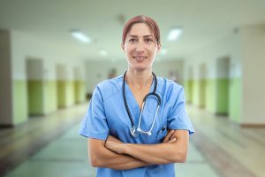 Female nurse wearing blue scrubs and standing in a hospital hallway