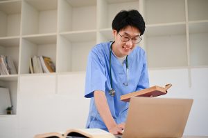 Male nursing student wearing scrubs and looking something up on the computer. 