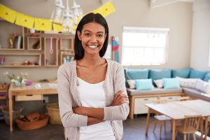 Female preschool teacher standing and posing in the middle of her empty classroom 
