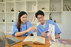 Male and female nursing students wearing blue scrubs and sitting at a table studying together.