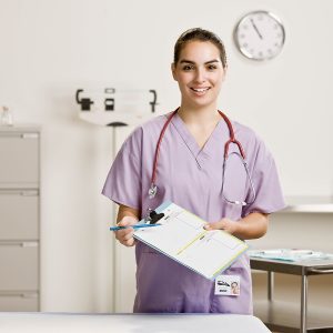 Female nurse wearing light purple scrubs and holding a medical chart and pen in her hands