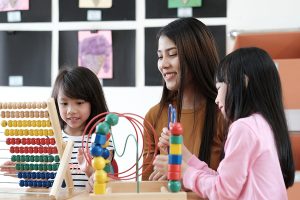 Female preschool teacher helping two young students with an activity.  