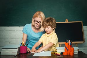 Preschool teacher working one on on with young student at her desk. 