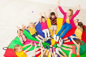 Preschool teacher sitting in a circle on a colorful parachute with her students, playing a game.