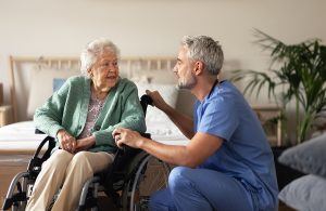 Male nurse talking to a female senior patient in a wheelchair in her home. 