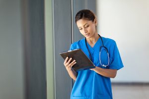 Female nurse wearing blue scrubs and holding a tablet in a hospital